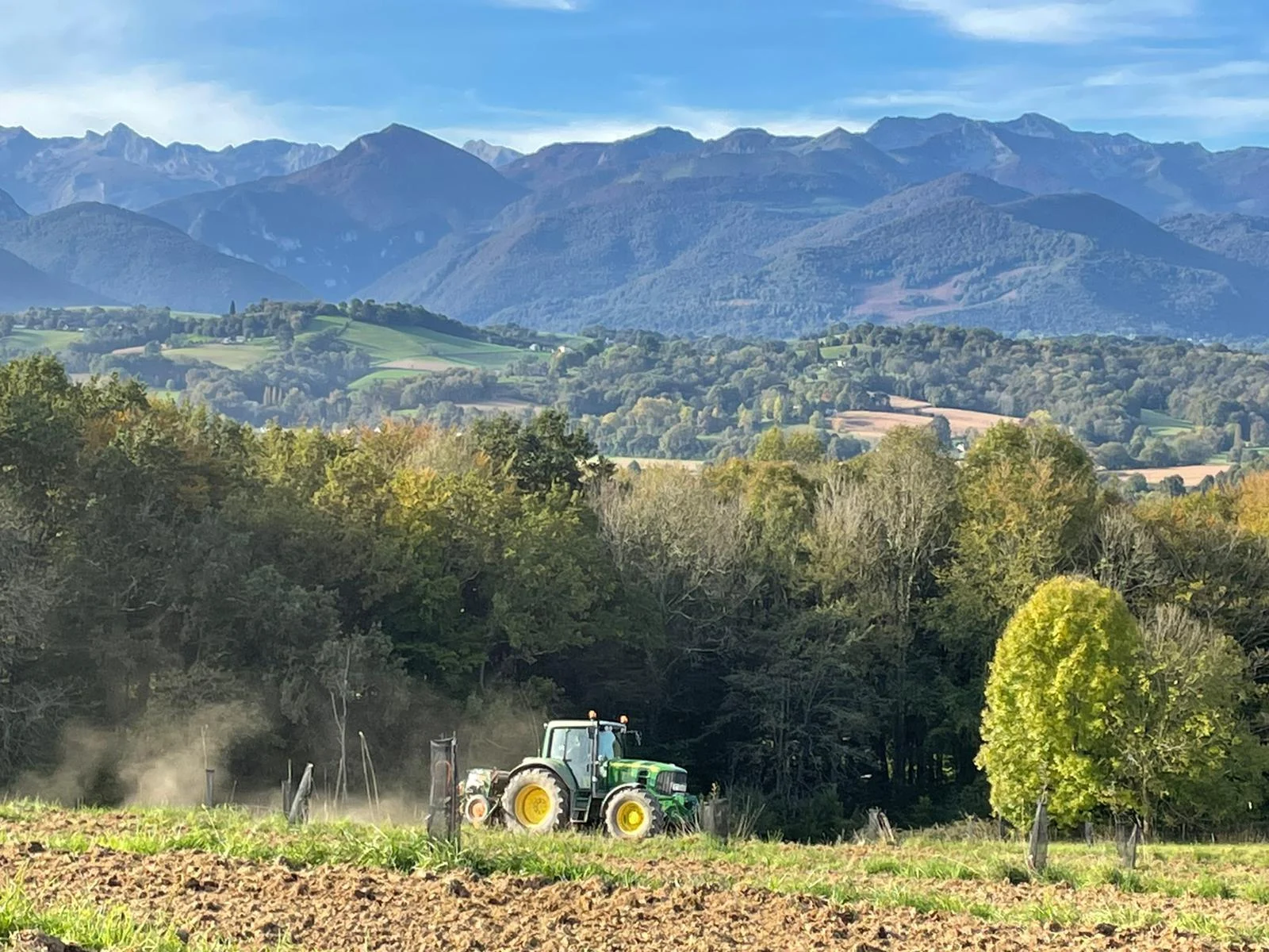 A tractor at work in a field, with the Pyrenees mountain range behind