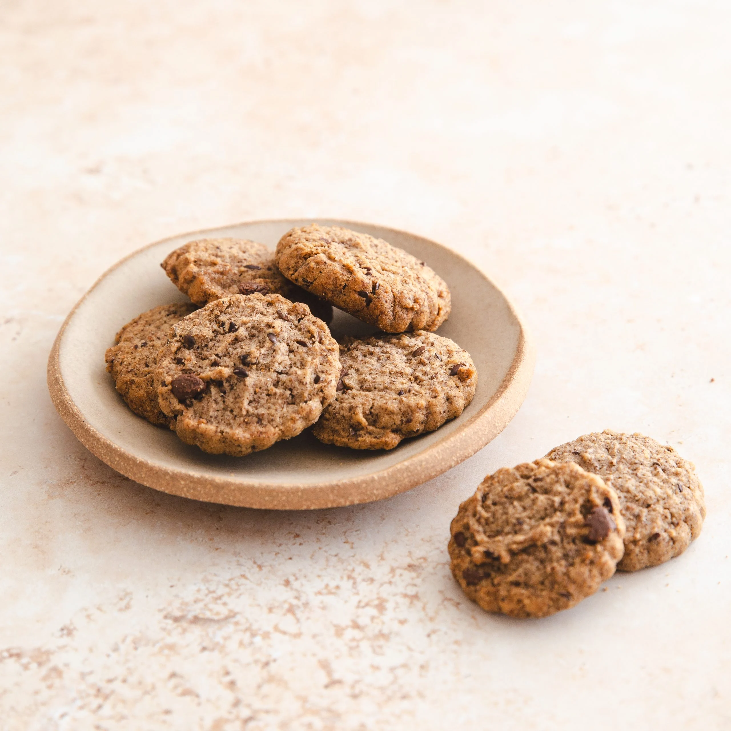Flax and chocolate chip biscuits in a stoneware dish, on a cream background